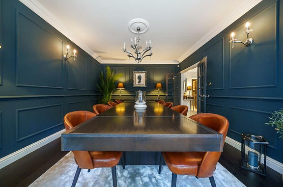 A bold blue dining room with a black table and brown leather chairs