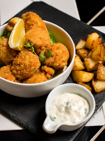 Un bol de croquettes dorées servies avec des potatoes et une sauce blanche au restaurant ALMA à Tunis.