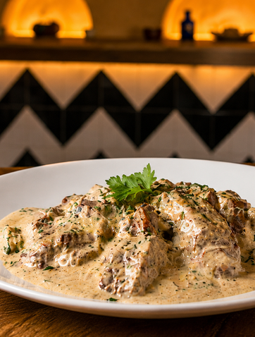 Un plat de viande en sauce crémeuse servi avec une bière pression fraîche au restaurant ALMA Tunis.