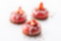 Drei glänzende rosa Desserts auf Keksboden, mit frischen Erdbeerscheiben und weißen Zuckerherzchen dekoriert.