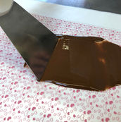 Spachtel verteilt flüssige Schokolade über eine Folie mit rosa Herzchenmuster.