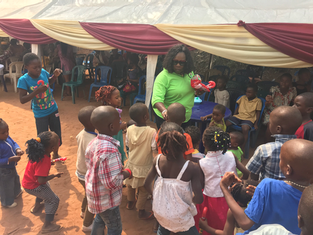 A woman in neon green passing out candies to small children in rural subsaharan Africa.