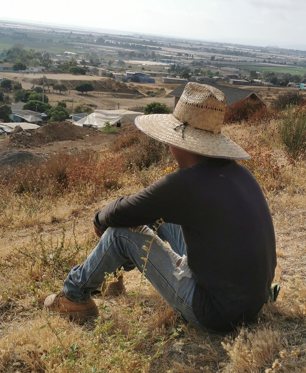 Sami, my man, sitting on a mountain or hill looking out, wearing. ahat