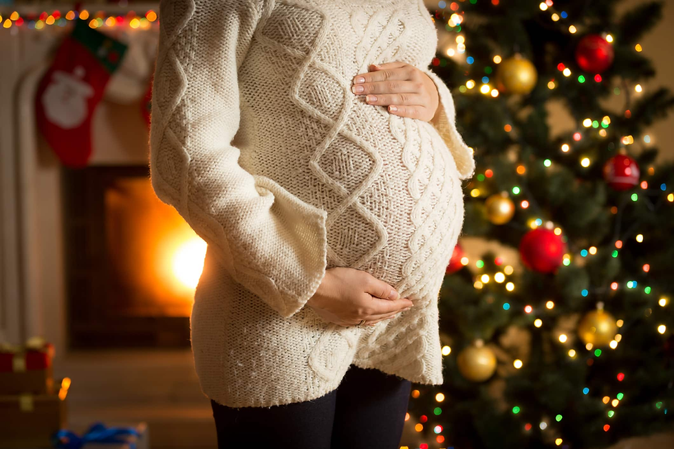 Pregnant woman standing in front of a decorated Christmas tree, embracing the holiday spirit while celebrating her pregnancy.