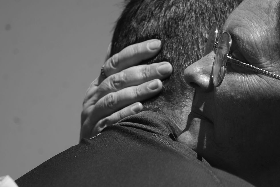 Main posée sur la nuque lors d’une étreinte, en noir et blanc, symbole d’accompagnement, de soutien et de transmission entre générations.