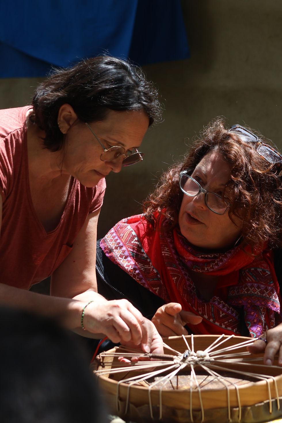 Deux femmes concentrées sur la création d’un tambour chamanique traditionnel lors d’un atelier en pleine lumière au Kenya, dans le cadre d’une retraite de fabrication de tambours en terre Maasaï, proposé et animé par Sylvie Di Scala