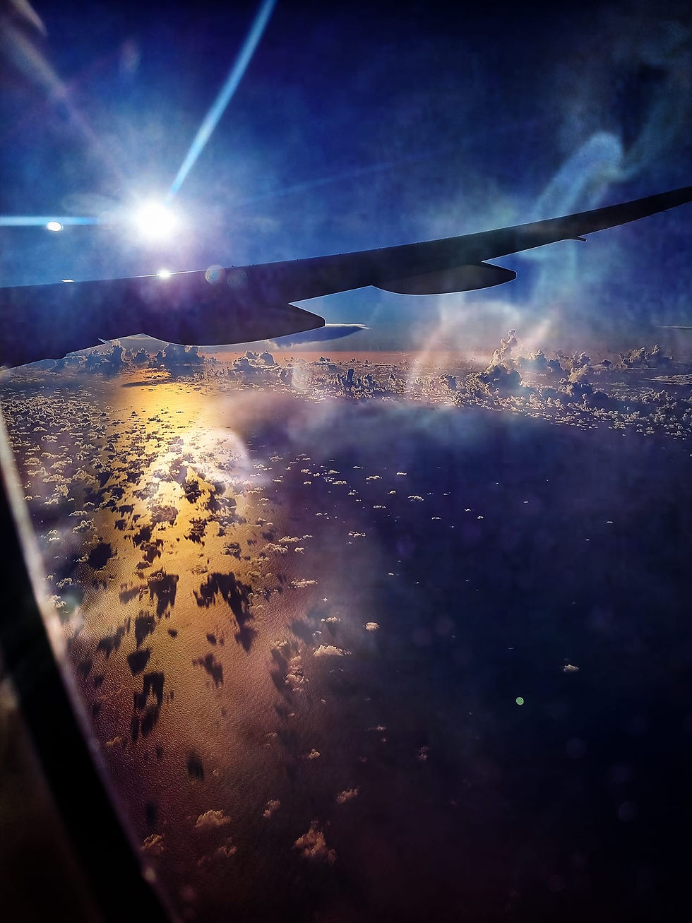 Vue aérienne d'un avion, vol au-dessus de la mer. On voit un petit bout du hublot en bas à gauche, également en haut l'aile droite de l'avion dans l'ombre. Au-dessus un ciel bleu nuit et le soleil qui se couche, il reste très brillant d'un blanc scintillant, des rayons partent vers le haut. Vers le bas, la mer et des moutons de nuages. La mer est teintée de jaune (soleil couchant) et d'un bleu profond à droite. Au centre, suite à un montage photo, apparaît en filigrane une chaîne brisée laissant entrevoir la liberté.