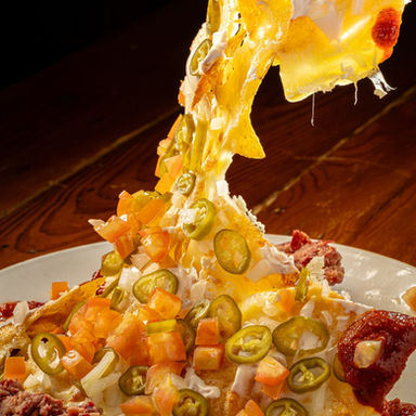 Loaded nachos piled high with jalapeños, fresh salsa, sour cream, and a generous pull of melted cheese at Jake's Charbroil Steaks.