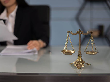 A focused view of the scales of justice on the desk of a woman reviewing legal documents.
