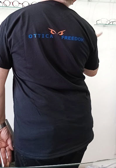 Uomo con maglietta nera Ottica Freedom davanti a una vetrina di occhiali.