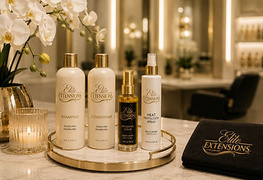 Elite Extensions branded hair care product line, including shampoo, conditioner, argan oil serum, and heat protection spray, displayed on a gold tray