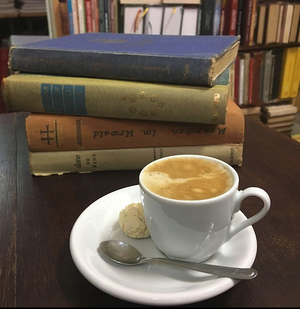 um café em uma xicara branca em uma uma mesa com livros
