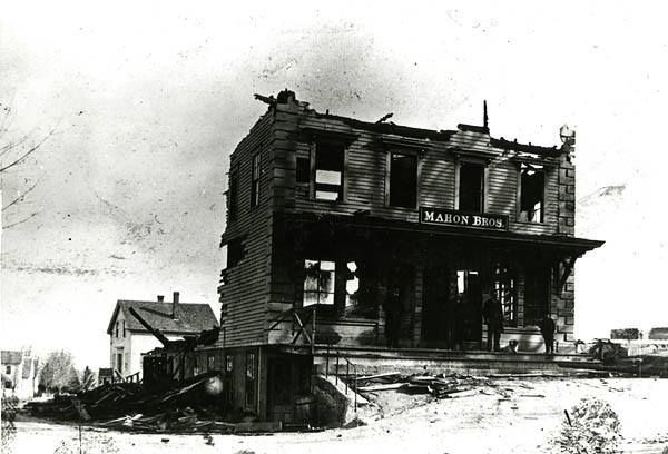 Two men and a dog of front steps of a burned out commercial building on the north side of Main Street in Hopkinton. The rear of the building is completely demolished but the Mahon Bros. sign is intact.... Photo Courtesy of the Hopkinton Public Library Treasure Room