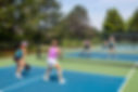 A competitive doubles game of pickleball at the net on a blue and green court in summer..j