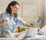 happy-casual-beautiful-woman-working-on-a-laptop-sitting-on-the-bed-in-the-house-stock-pho