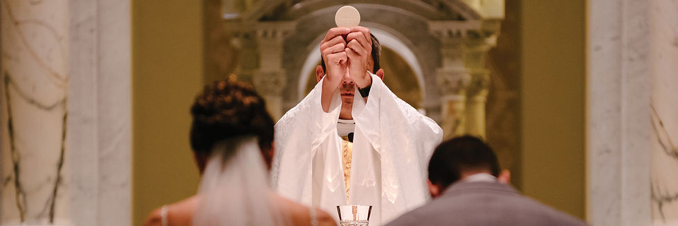 A priest holding the Eucharist as a bride and groom kneel in front of the altar