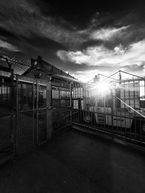 Industrial dockyard framed by fencing with piercing low sun and dramatic sky