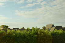 Countryside view from a moving train with rooftops and greenery under a soft sky
