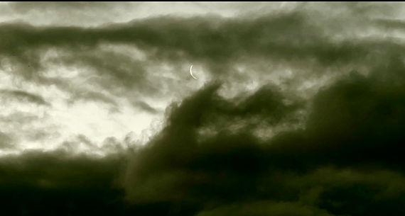 Image of stormy green skies with a sliver of the moon hidden peaking through the clouds