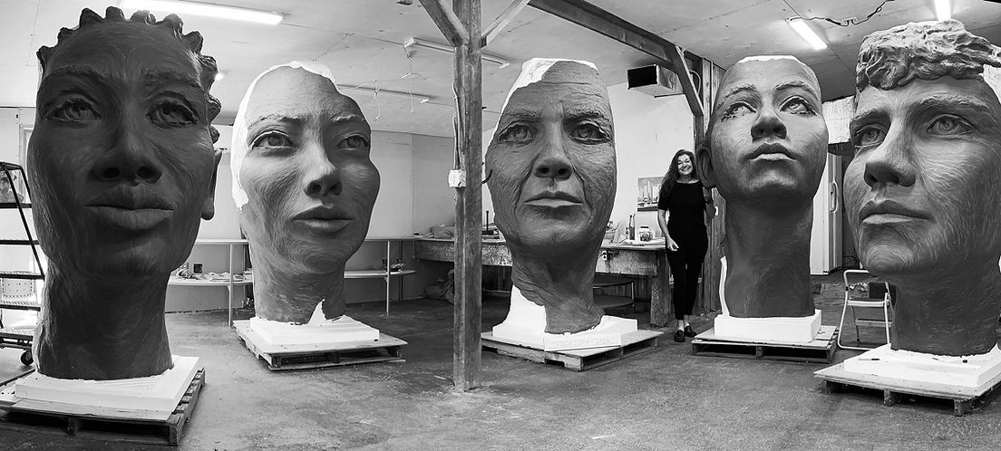 Amanda Matthews in studio with giant clay faces of the girl puzzle monument