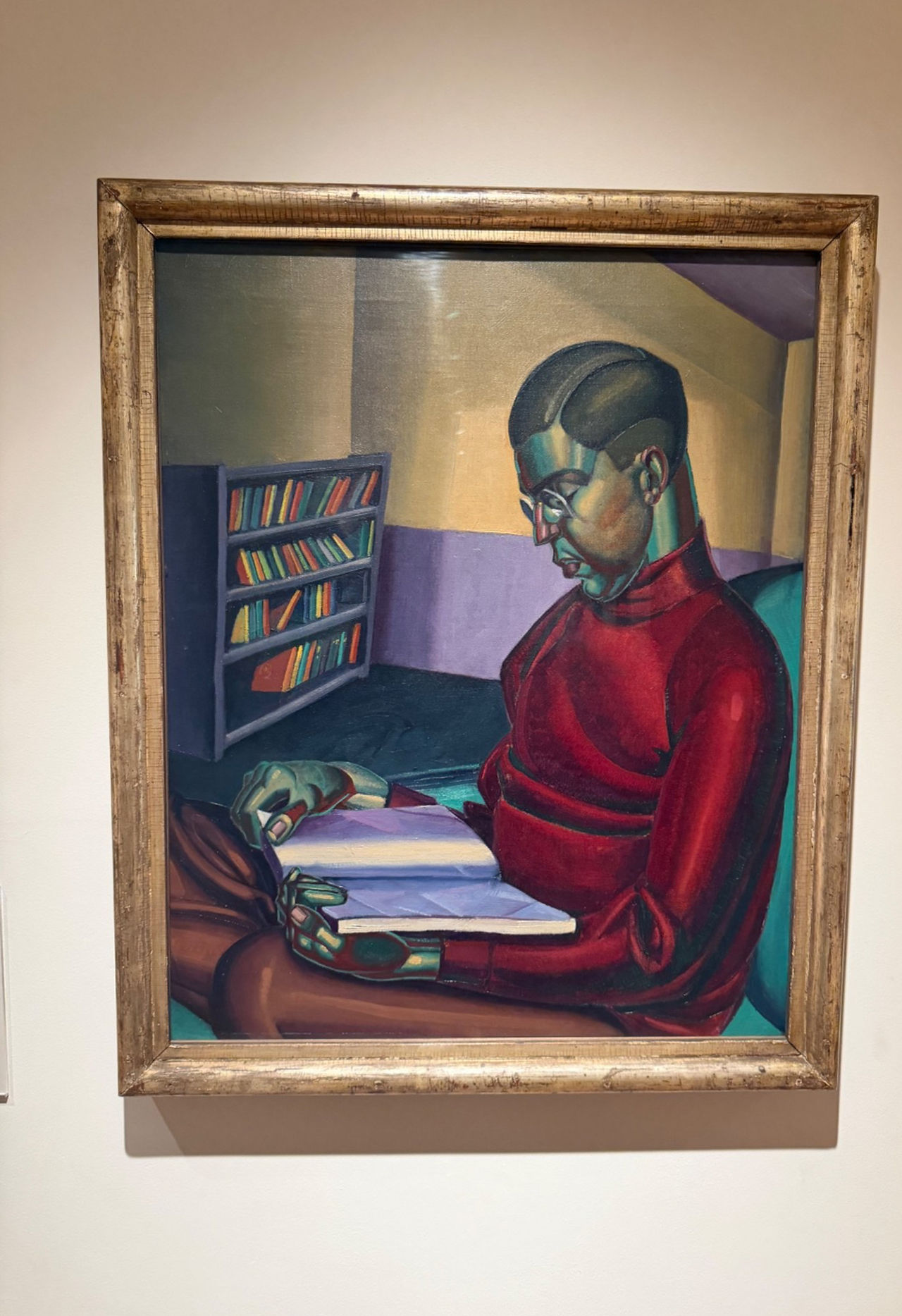 William McCance Portrait of Joseph Brewer 1925, modernist oil painting showing a seated man reading, with geometric forms and a deep red sweater, photographed in a gallery setting.