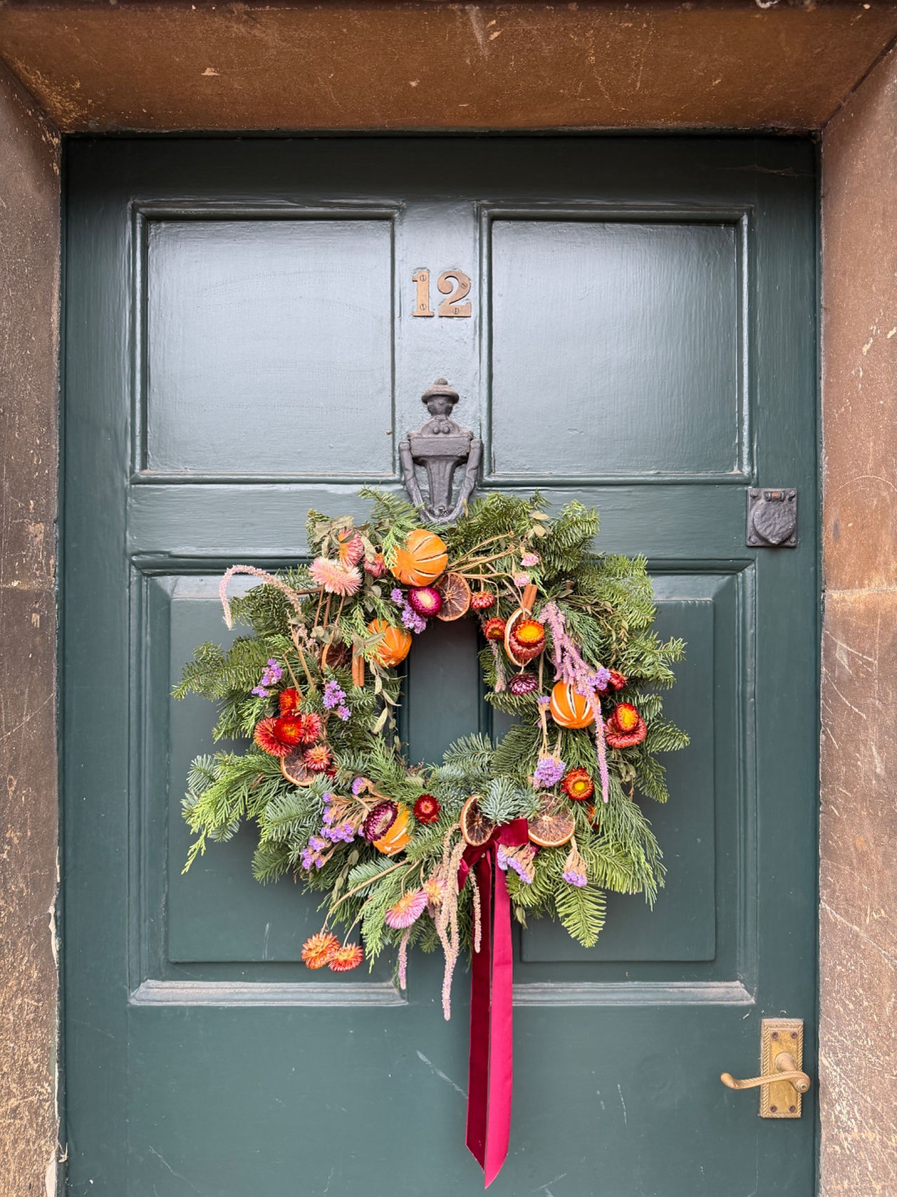 Green painted front door in Lacock, Cotswolds, decorated with a seasonal wreath of foliage, dried flowers and citrus