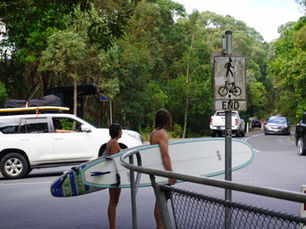 Two surfers carrying their boards and walking across the road towards the beach in Byron Bay, Australia.