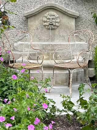 A pair of cast iron garden chairs and a French fountain.