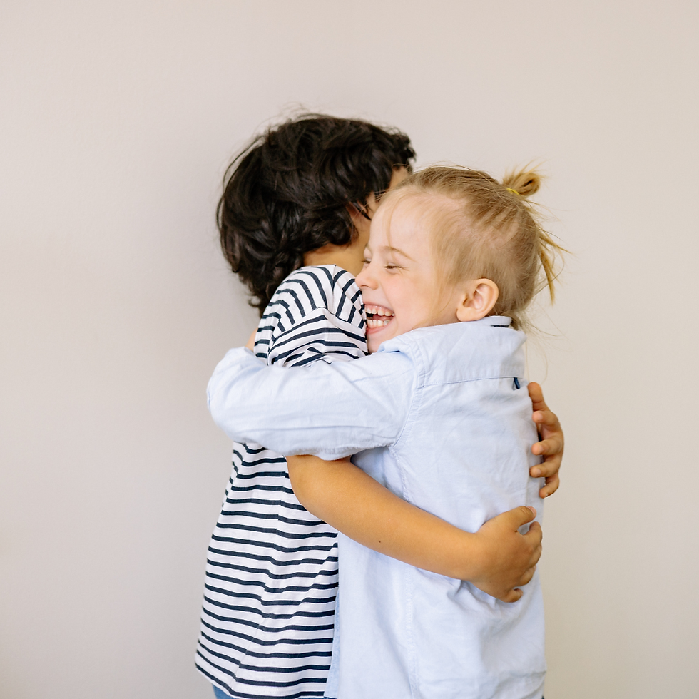 Two children hugging joyfully, one in a striped shirt and the other in a light blue shirt, against a plain beige background.