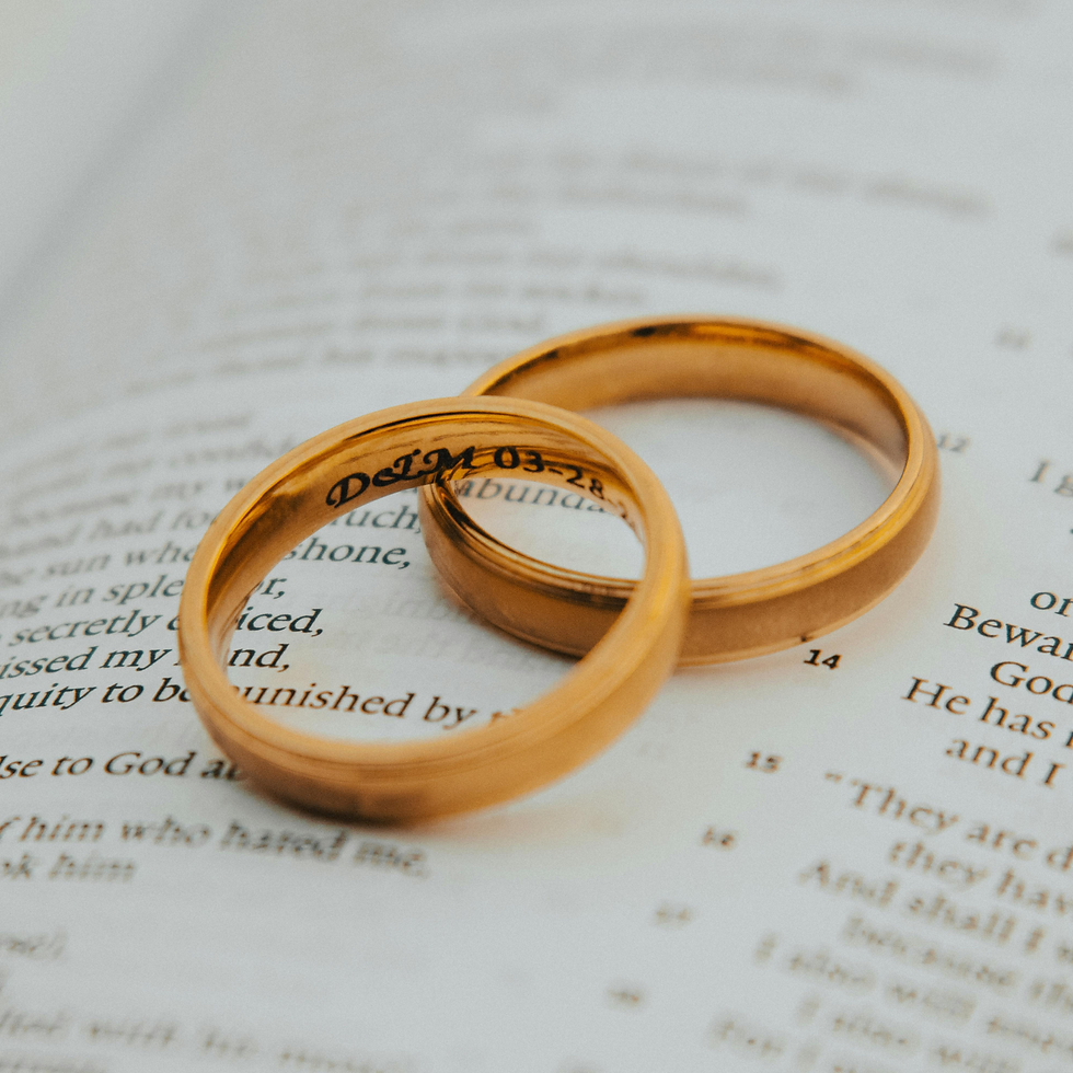 Two gold wedding rings resting on a book page with visible text, creating a romantic, intimate close-up scene.