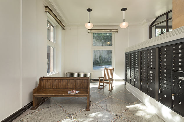 The Cambridge lobby has large windows, white walls, a marble floor. There are resident mailboxes in the center of the space and wooden benches along the left wall.