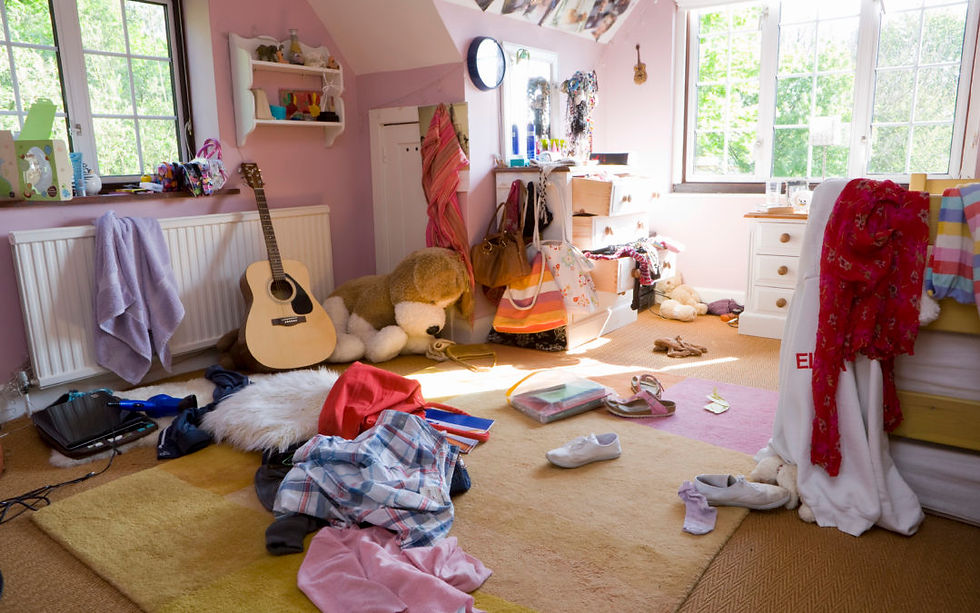 A cozy pink bedroom is scattered with clothes, toys, and a guitar, capturing a scene of everyday chaos and creativity.