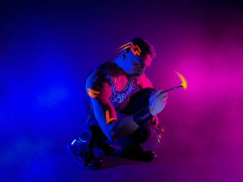artist sits with neon paintbrush in hand on a blue and purple backdrop