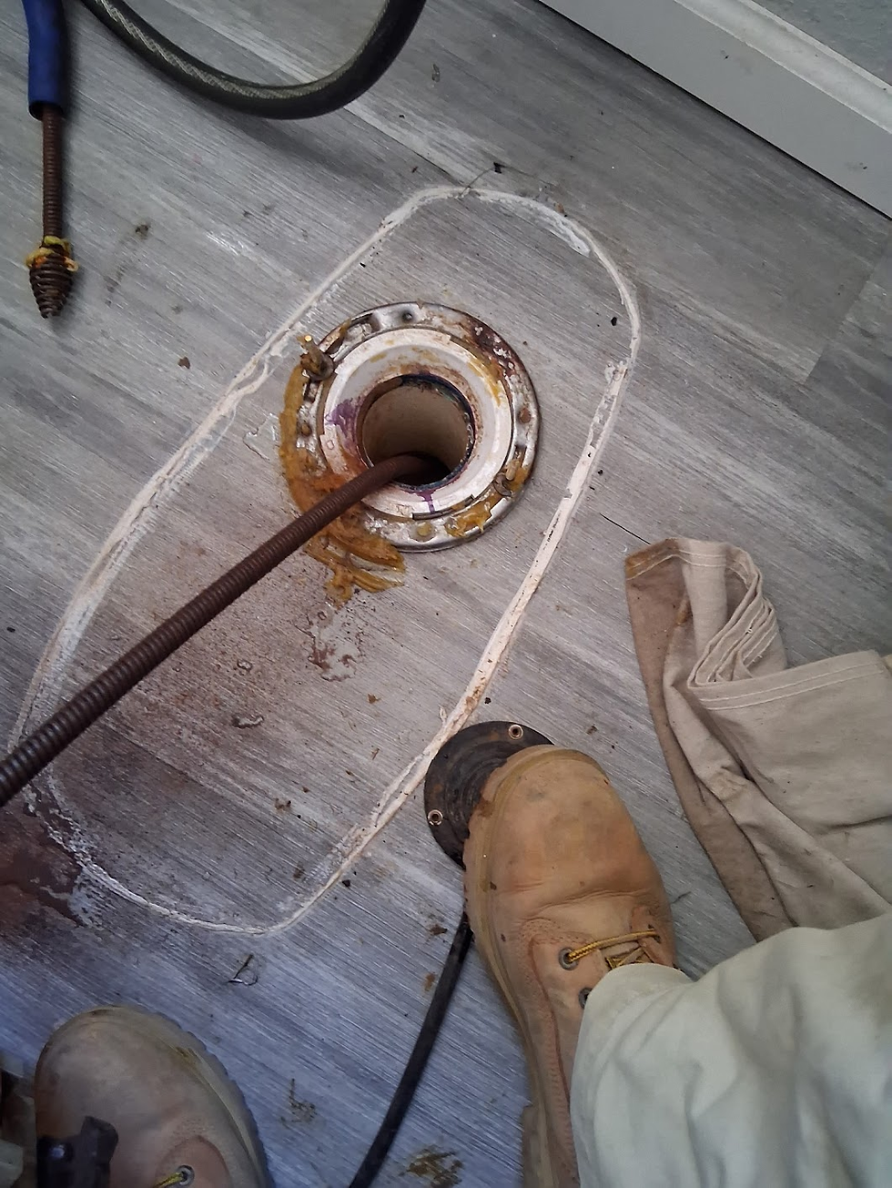 Plumber using a drain auger to clear a clogged main line through a toilet drain opening