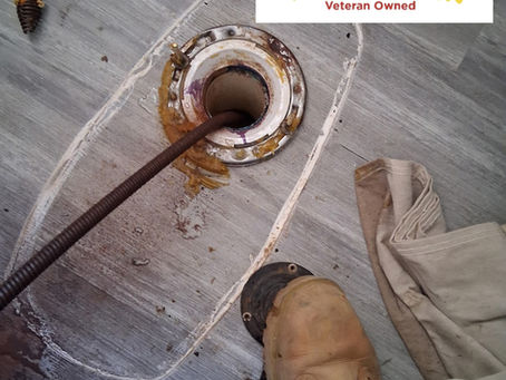 Plumber using a drain auger to clear a clogged main line through a toilet drain opening
