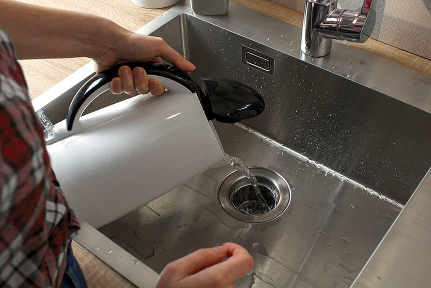 Pouring water into a kitchen sink drain to test for a clog or drainage issue