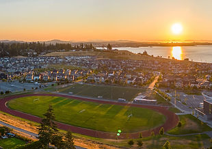 Aerial photograph of Royal Bay in Colwood, BC at sunset, showing the master-planned community alongside Royal Bay Secondary School and the Salish Sea