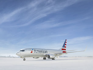 Close-up profile view of an American Airlines passenger airplane against a bright blue sky with light, wispy clouds.