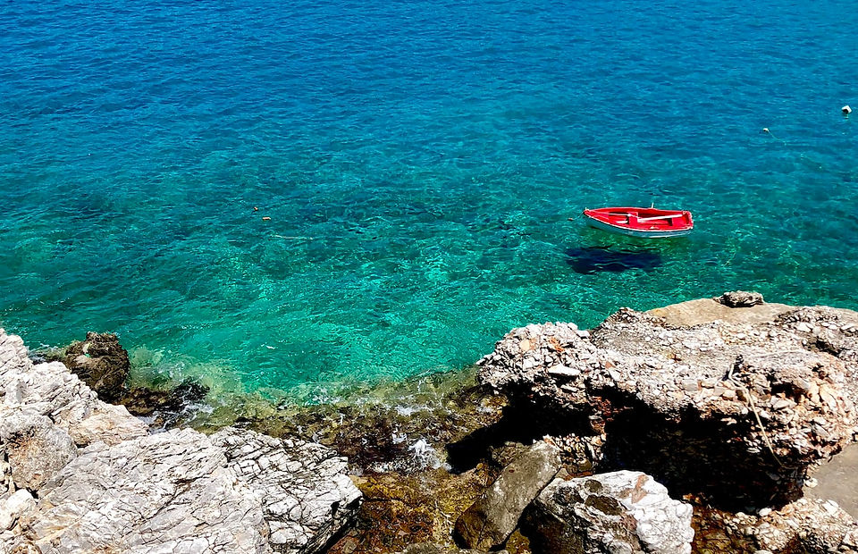 A bright red boat anchored in the turquoise waters of Folegandros, surrounded by stunning cliffs and colorful buildings in the distance.