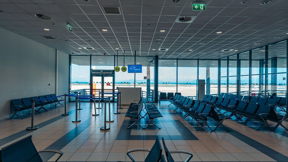 Inside a bright, modern departure gate waiting area at Rhodes International Airport (RHO). Rows of empty blue chairs are arranged on a tiled floor under a gridded drop ceiling with recessed lighting. Large floor-to-ceiling glass windows look out toward the bright tarmac and the blue sea in the distance. Blue stanchion ropes define a queuing line near gates 9a and 9b, which feature a Fraport branded digital flight information screen.