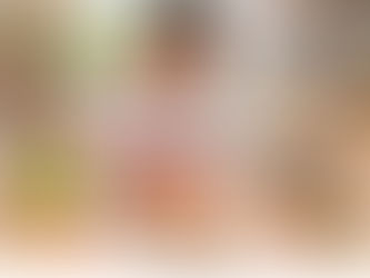 Smiling girl arranges red blocks at a wooden table with apples, toy cars, bears, crayons, and oranges in a bright classroom-like room
