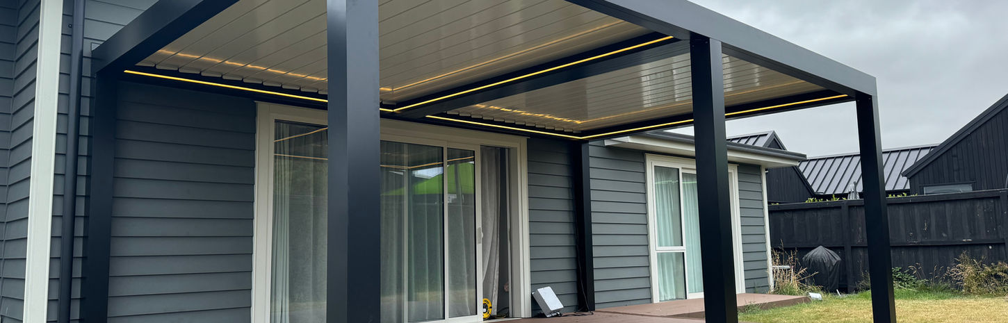 A closed white Skyline Louvre above a deck. The deck and Skyline Louvre are attached to a blue house with French doors that open onto the patio. 