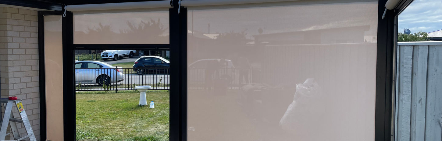 Partially closed cream outdoor blinds enclose a pale wood deck.