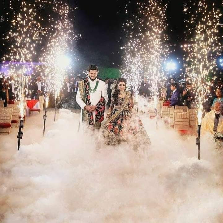 Couple walks through sparklers; celebratory scene with smoke and lights.
