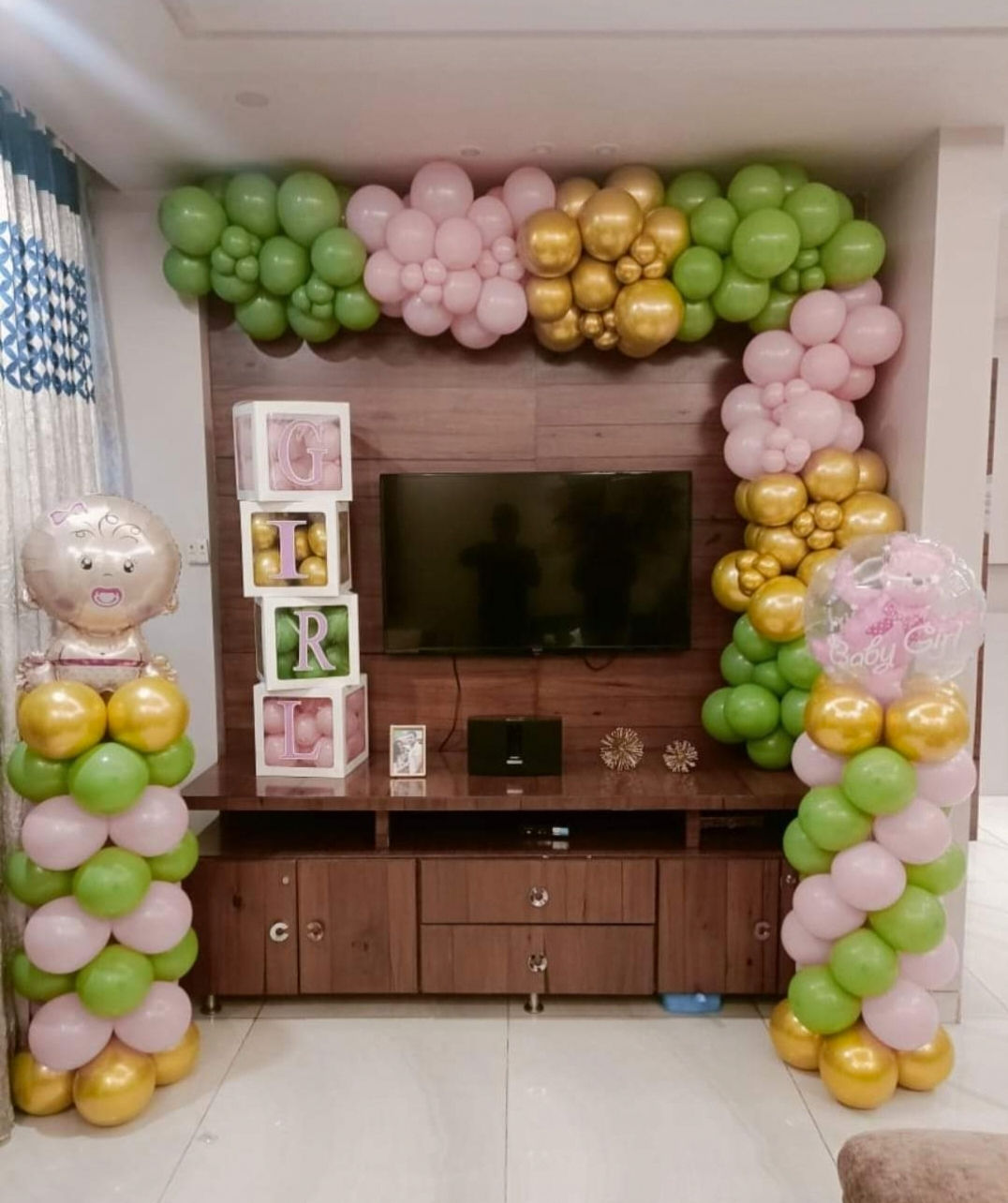 Green, pink, and gold balloons decorate a wall, decor Oh Baby Pastel Themed Decor SKU307, with a TV.
