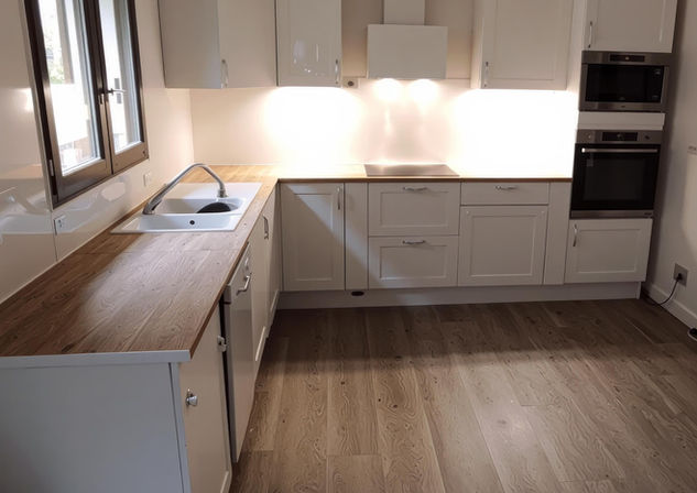 Cuisine aménagée avec armoires blanches et plan de travail en bois.