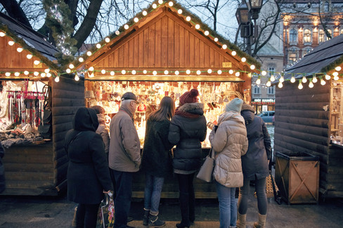 People gathered at a festive Christmas market, enjoying holiday decorations, lights, and seasonal treats.