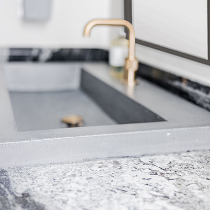 Modern concrete trough sink with gold faucet.