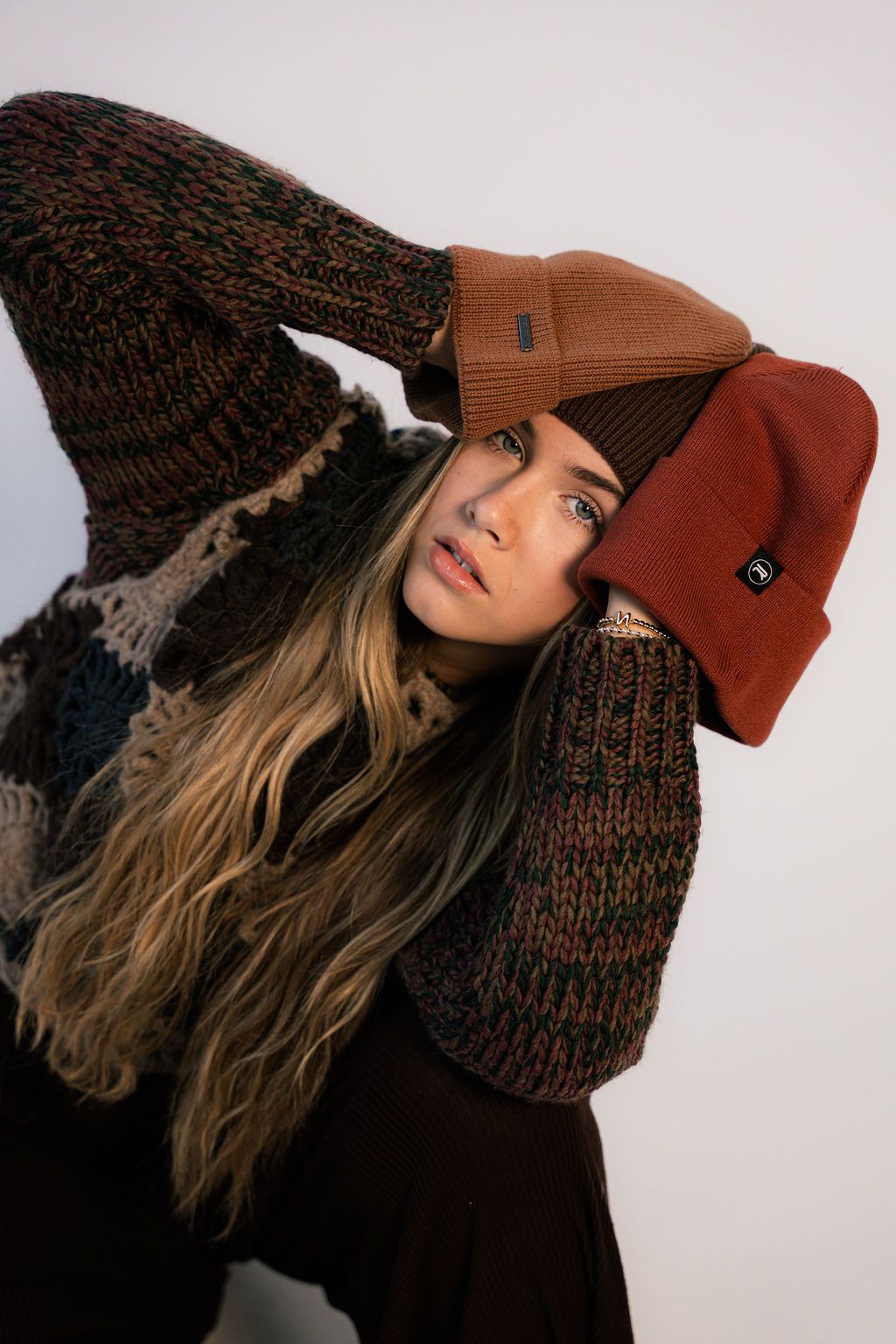 Woman holding three Revony beanies in tan, brown and rust