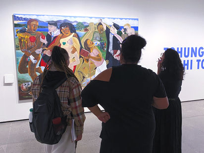 Three wāhine standing with thier back to the camera, looking at Robyn Kahukiwa's painting